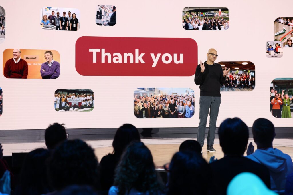 icrosoft CEO Satya Nadella on stage thanking employees during the company's 50th anniversary presentation, with team photos displayed in the background