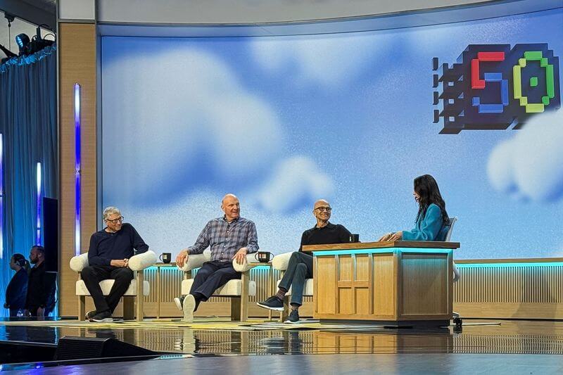 Bill Gates, Steve Ballmer, and Satya Nadella speaking on stage during Microsoft's 50th anniversary event, hosted in a modern tech panel setting.
