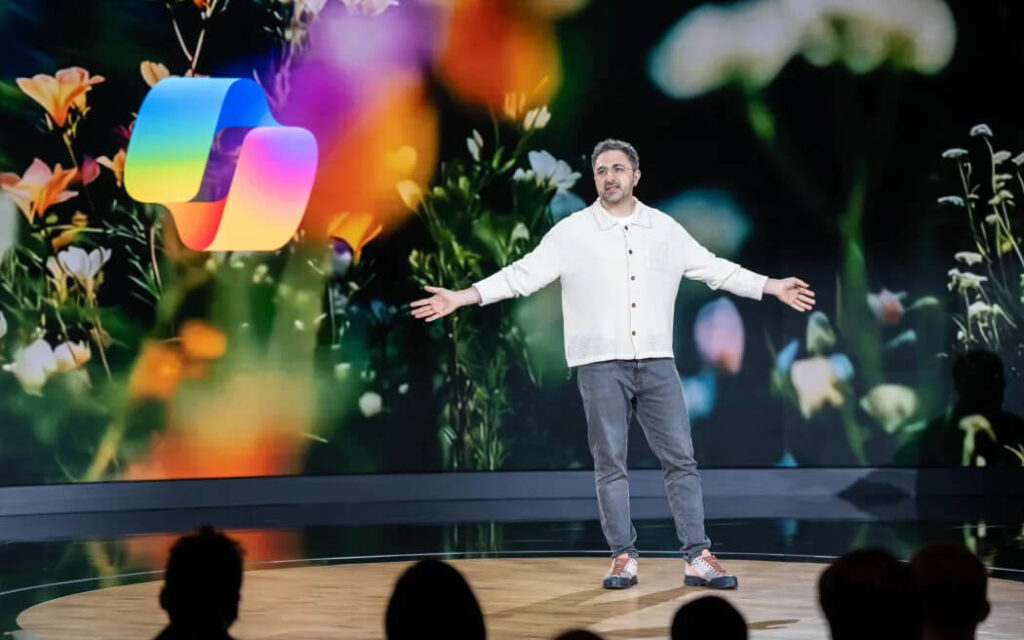 A Microsoft speaker presenting on stage in front of a vibrant floral background with an AI-themed logo during a keynote session.